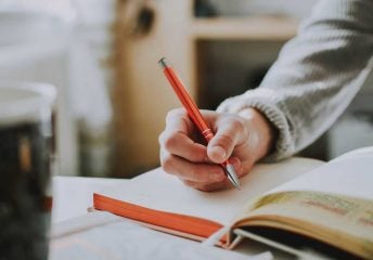 Image of someone holding a pen and writing in a notebook.